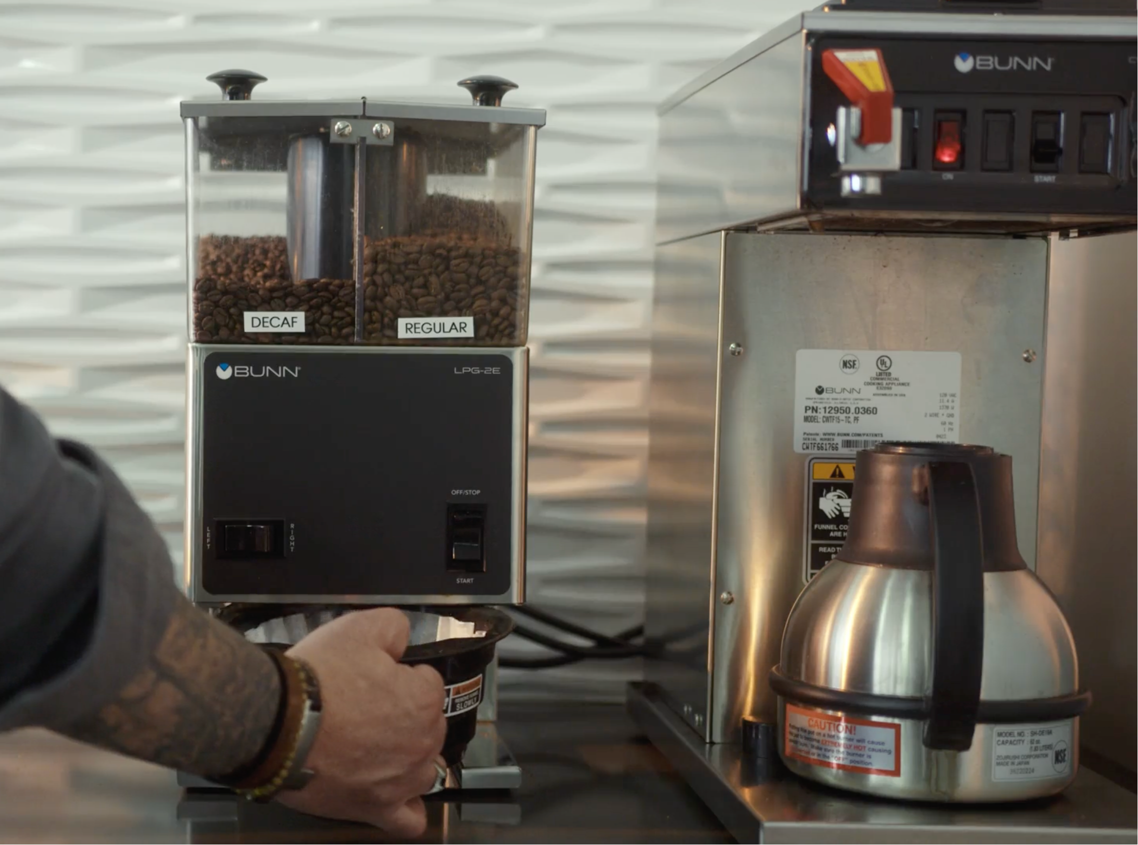 Bunn coffee grinder and coffee maker with a person's hand interacting with the grinder.