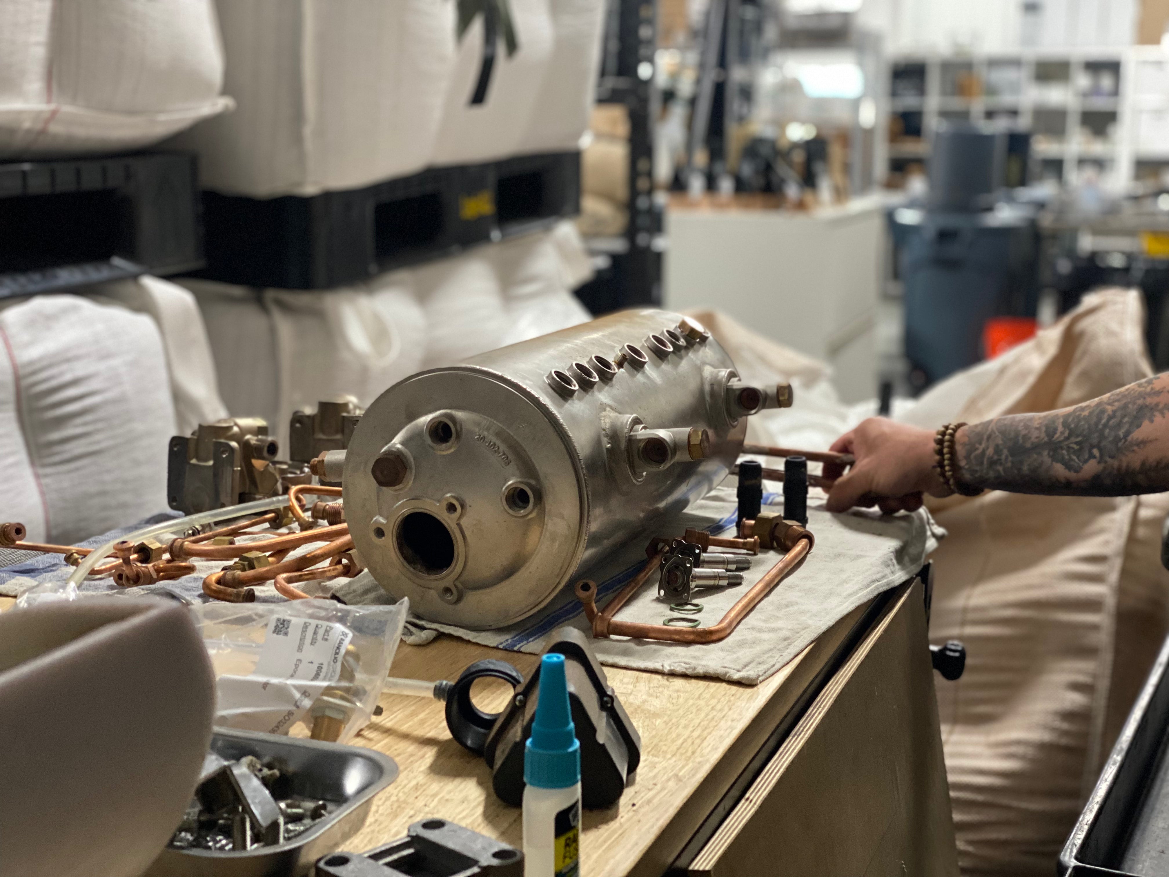 Tattooed arm working on disassembled espresso machine component parts